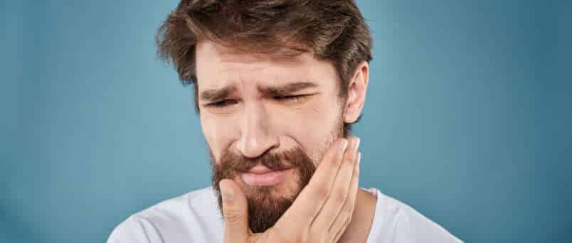 a man holding his cheek as he's suffering from meth mouth sores