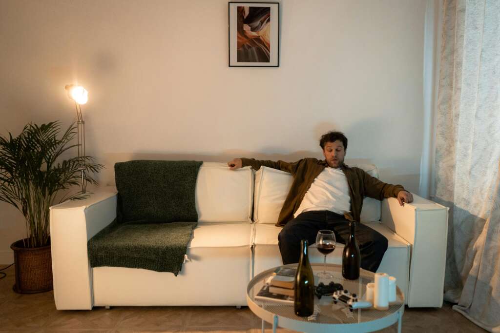 a man sitting on the couch drinking and experiencing the drunk stage.